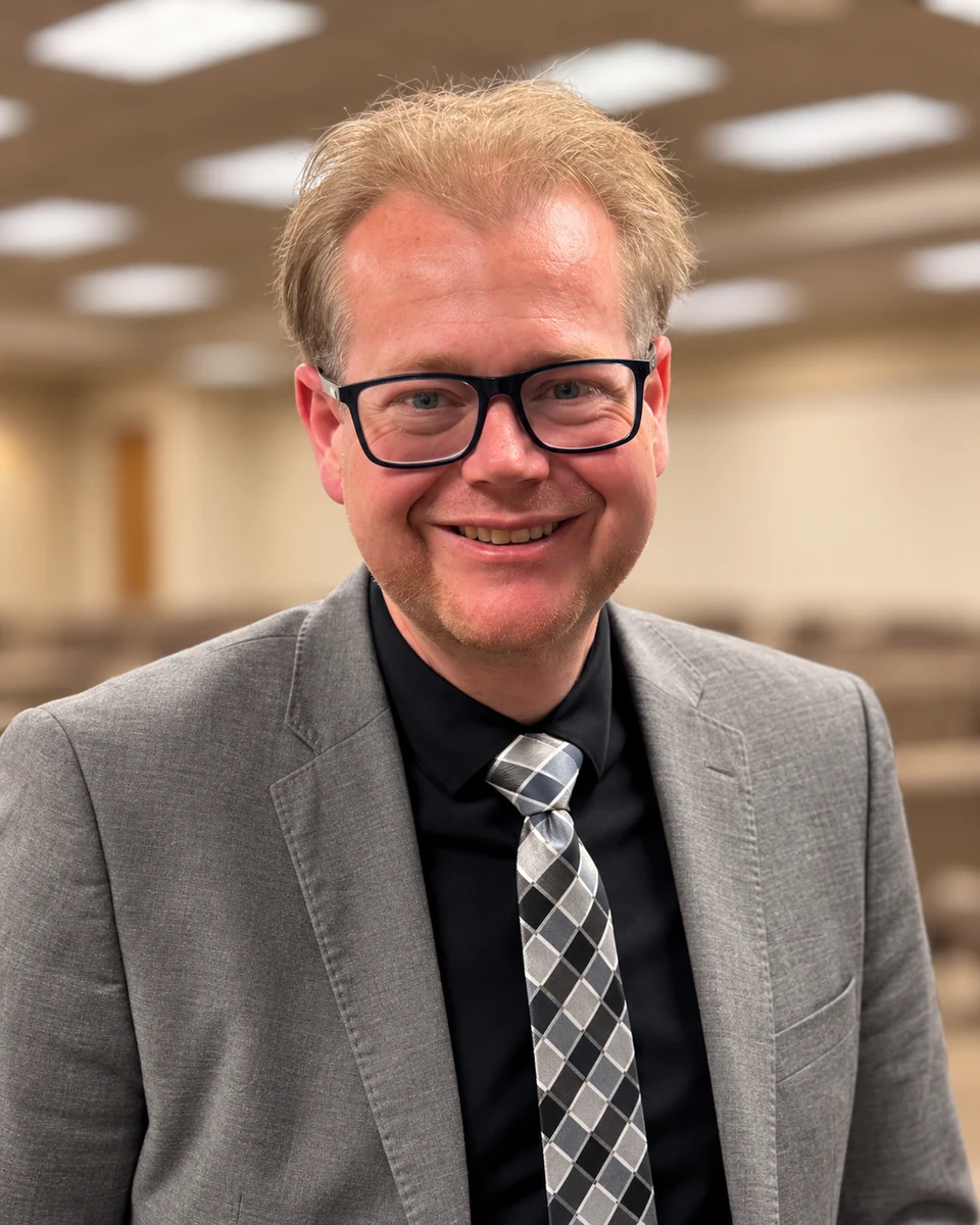 David Buynar smiling, wearing glasses and a gray suit